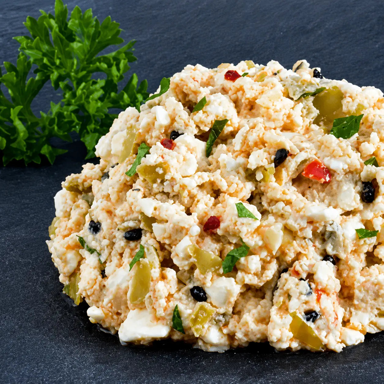 Griechischer Obatzda von Antipasti-Versand mit Schafskäse, Oliven und Paprika auf dunklem Schieferuntergrund