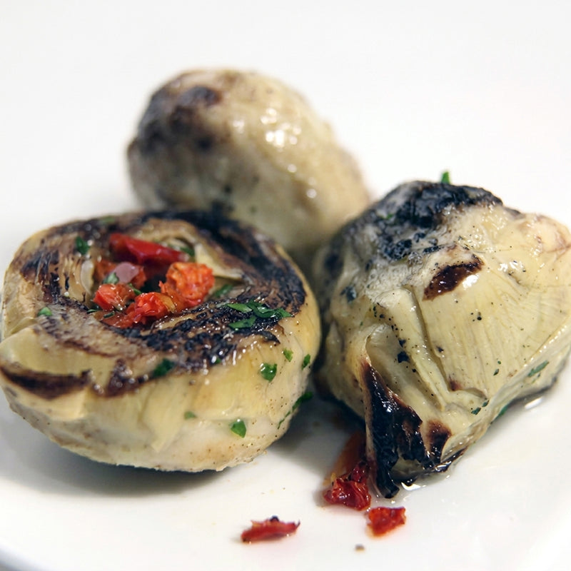 Gegrillte Artischockenherzen mit Röstnote, halbiert auf einem Teller, mit Kräutern und Paprika